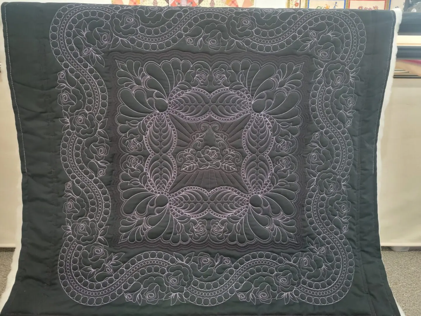 A square quilt with a design of leaves and swirls.