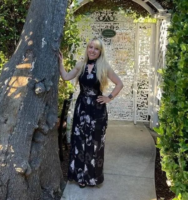 A woman standing next to a tree in front of a gate.